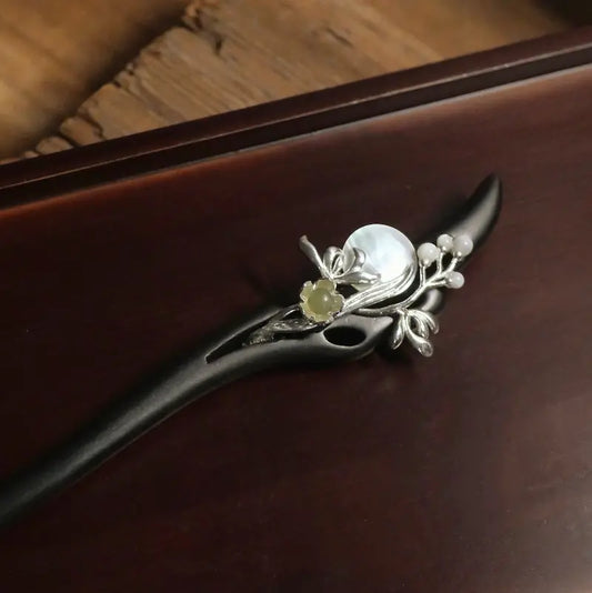 An elegant close-up of the carved green nephrite jade blossom and iridescent pearl disc set on silver-plated branches against a dark wooden background.