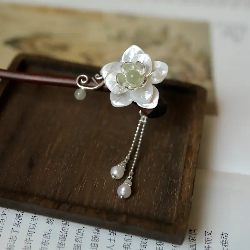 An exquisite micro close-up focusing on the layers of natural mother of pearl shell craft and the smooth, round freshwater pearl drop tassels on a wooden stand.