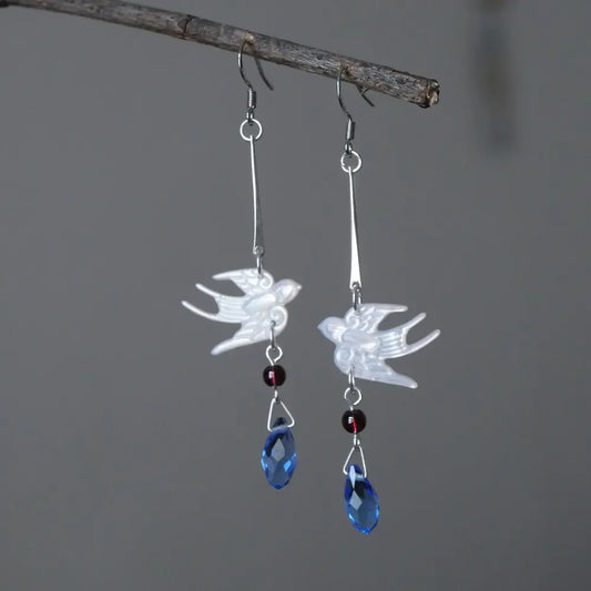 Silver mother of pearl swallow drop earrings with garnet beads and blue crystal teardrops hanging on a rustic branch — Orienlu