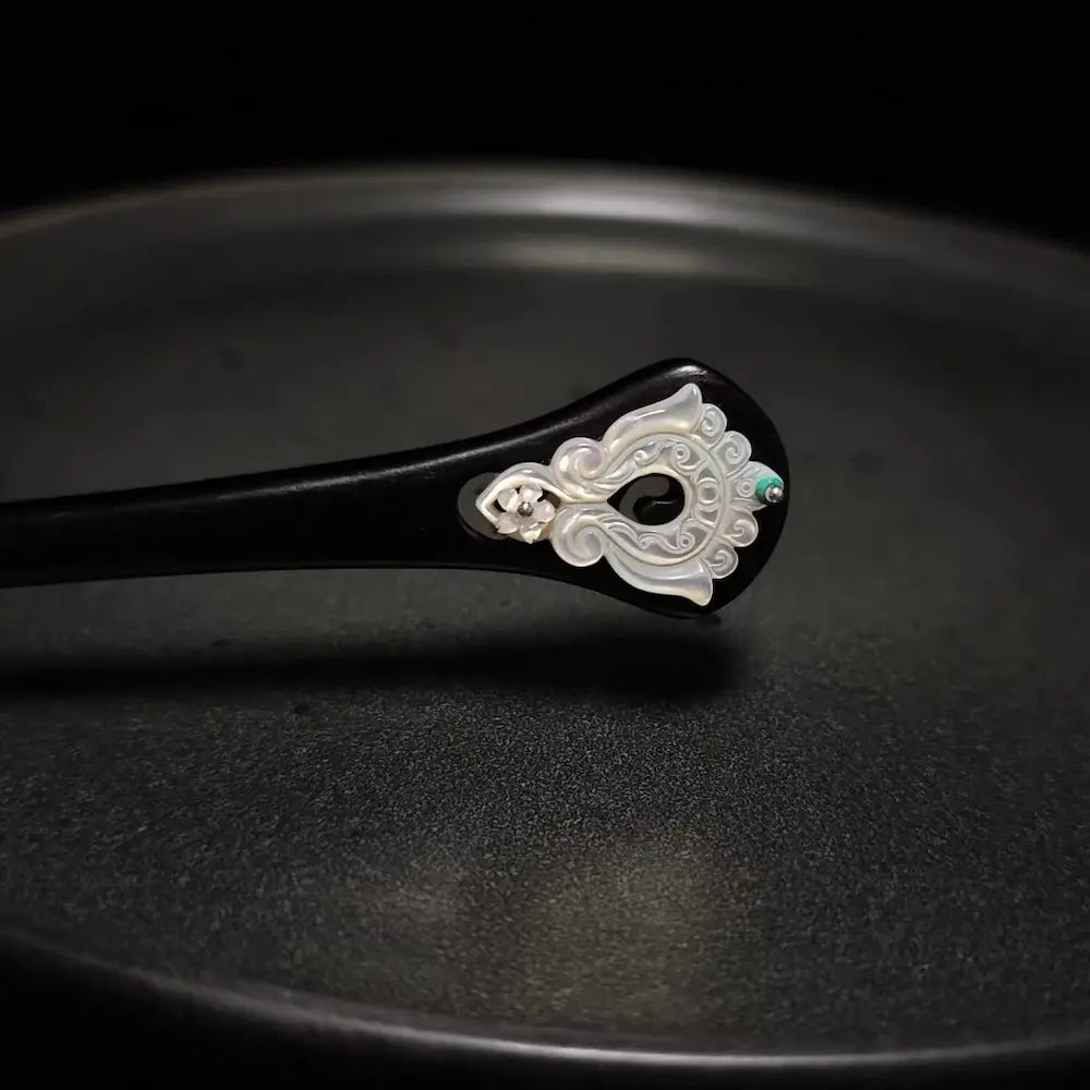 Close-up detail of the artisan carved mother of pearl shell and green gemstone inlay on the top of the black wooden hair stick.