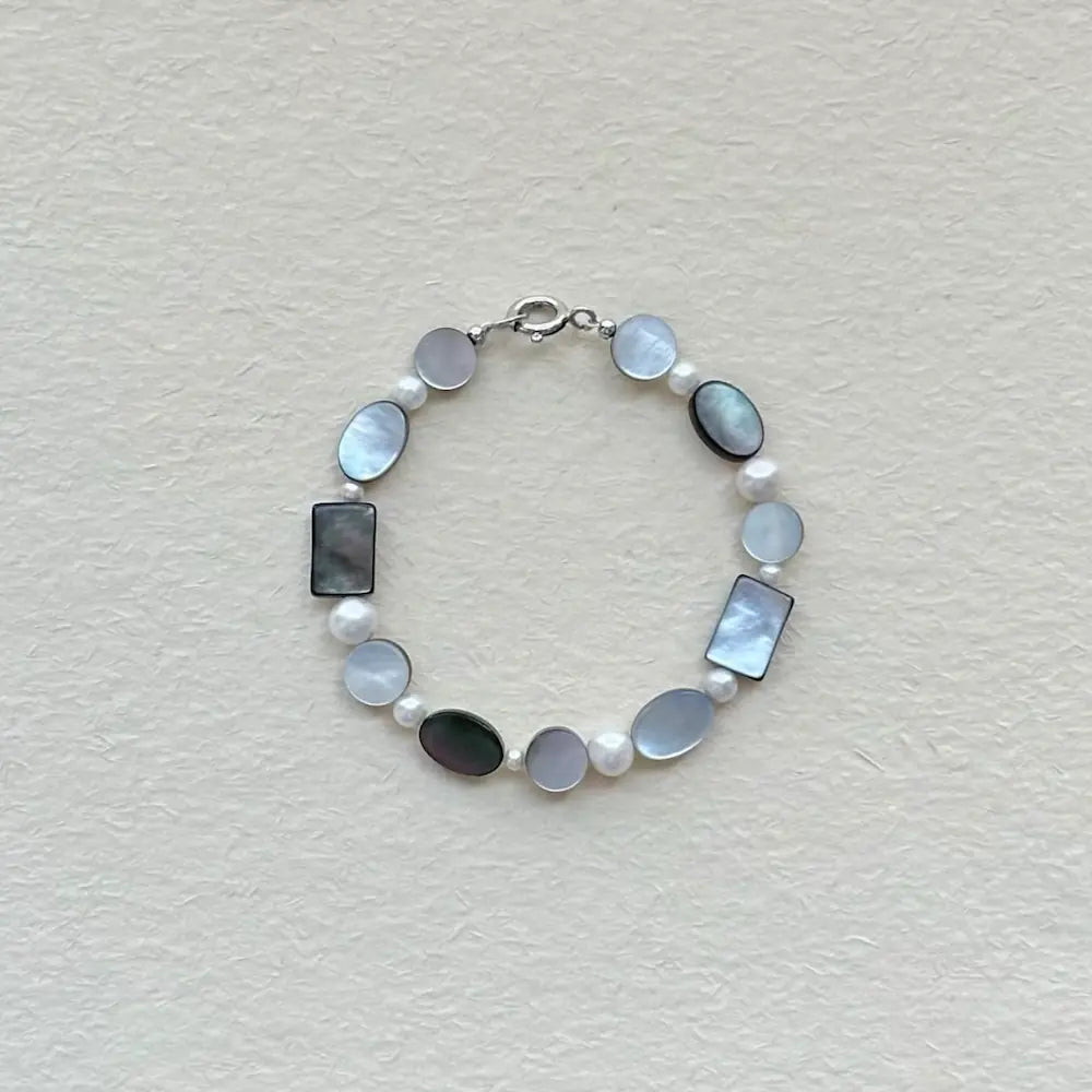 Handcrafted black mother of pearl and freshwater pearl geometric bracelet on textured paper surface Orienlu