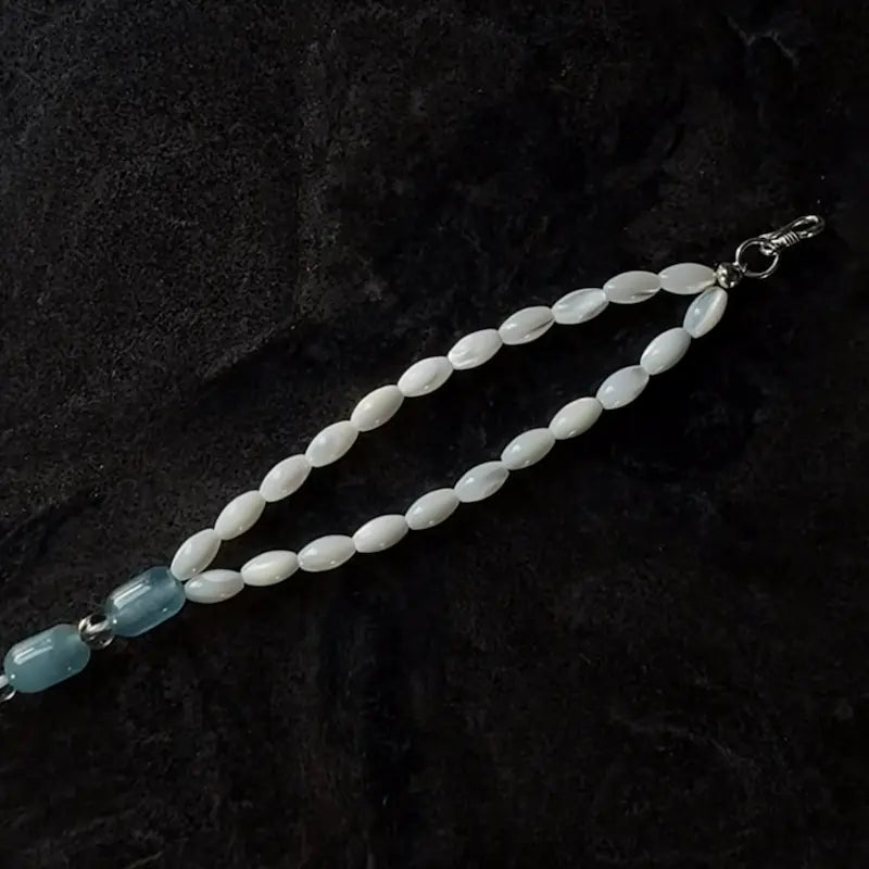 Close-up of white mother of pearl rice beads and silver S clasp on dark slate background Orienlu