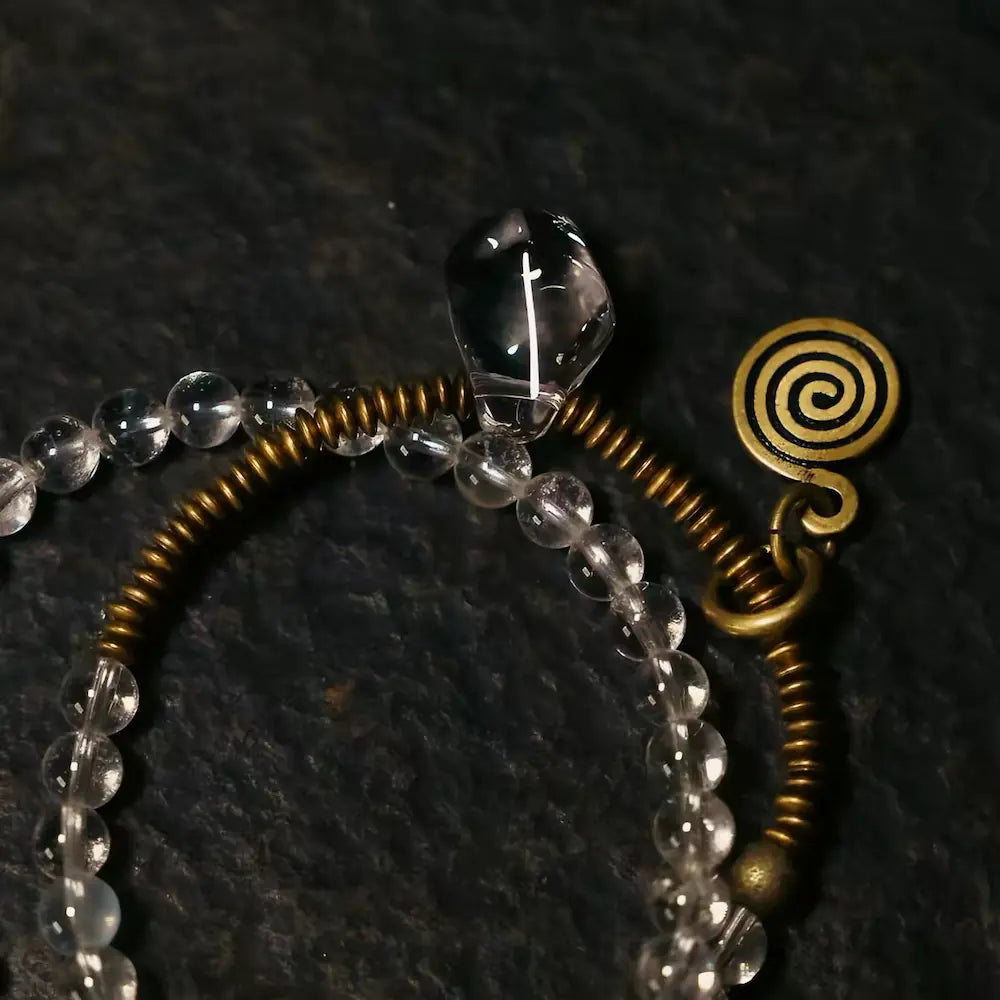 Close-up of copper coil spring and spiral shell pendant on clear quartz bracelet — Orienlu