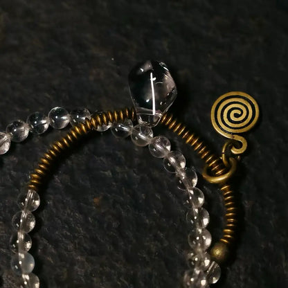 Close-up of copper coil spring and spiral shell pendant on clear quartz bracelet — Orienlu