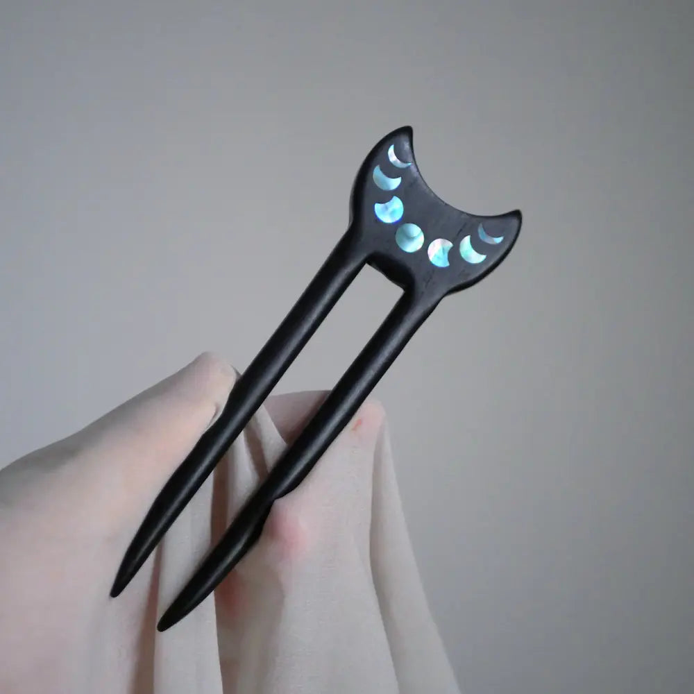 Ebony crescent moon phase hair fork held in hand against soft fabric Orienlu