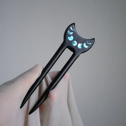 Ebony crescent moon phase hair fork held in hand against soft fabric Orienlu
