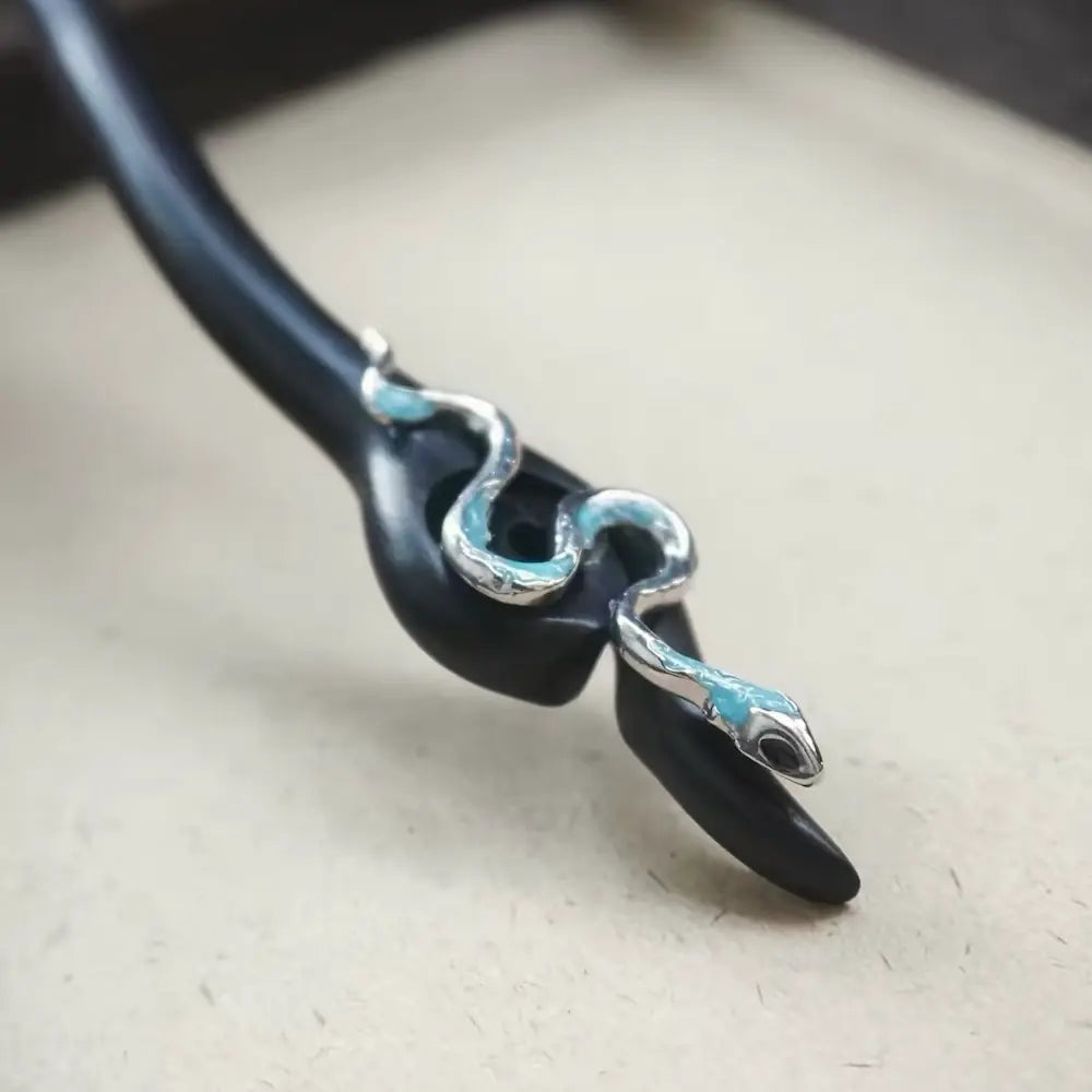 Close-up of silver-tone snake ornament with blue enamel accents on ebony hair stick Orienlu