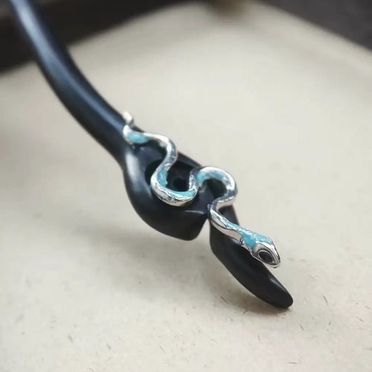 Close-up of silver-tone snake ornament with blue enamel accents on ebony hair stick Orienlu