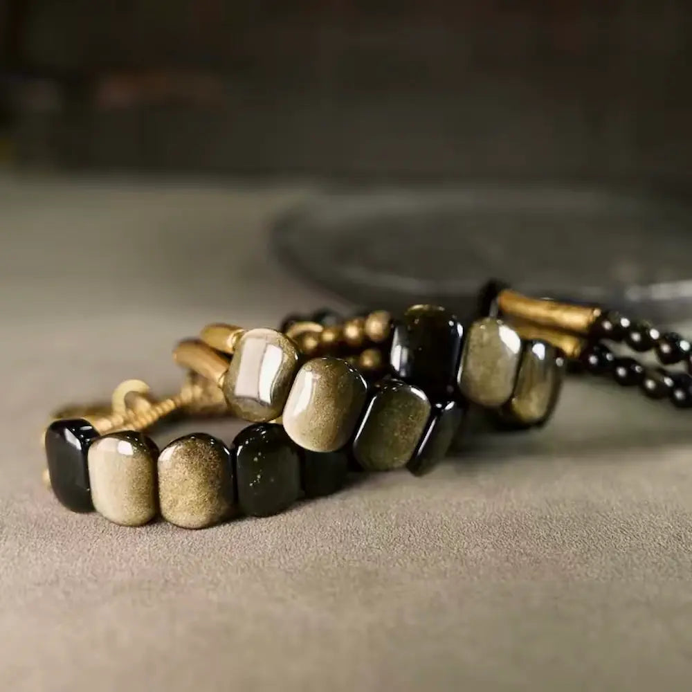 Two gold sheen obsidian protection bracelets stacked together on a grey surface showing metallic luster