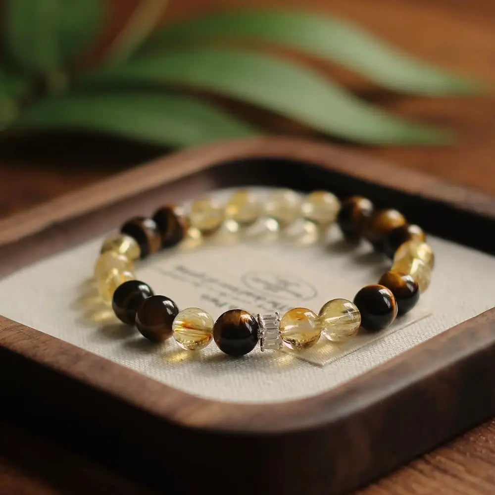 Two-tone citrine and tiger's eye gemstone bracelet displayed in a wooden tray with green leaves Orienlu