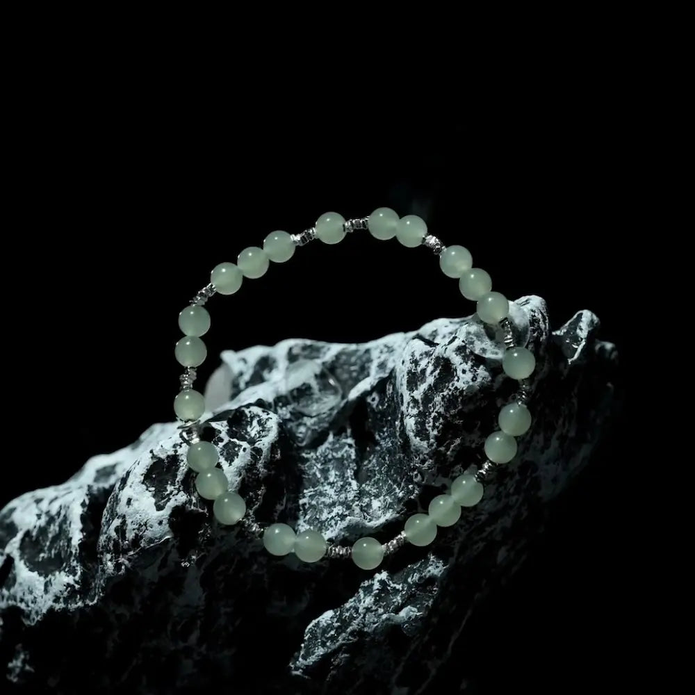 Pale green hetian jade bracelet displayed on black and white stone in dramatic lighting Orienlu