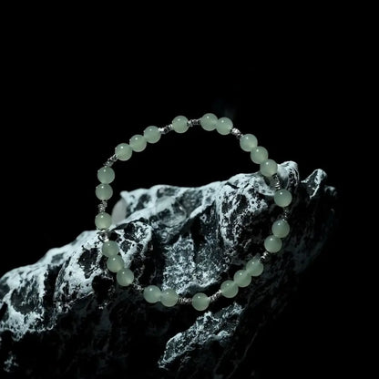 Pale green hetian jade bracelet displayed on black and white stone in dramatic lighting Orienlu