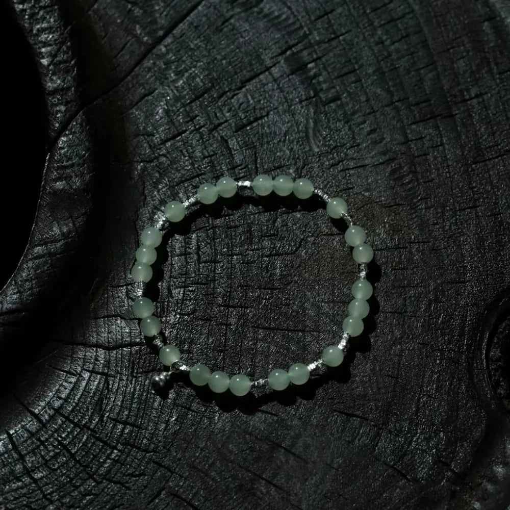 Handcrafted hetian jade bracelet with pale green beads and titanium gourd pendant on dark textured wood surface Orienlu