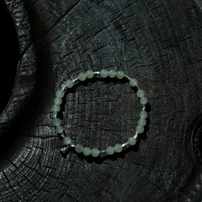Handcrafted hetian jade bracelet with pale green beads and titanium gourd pendant on dark textured wood surface Orienlu