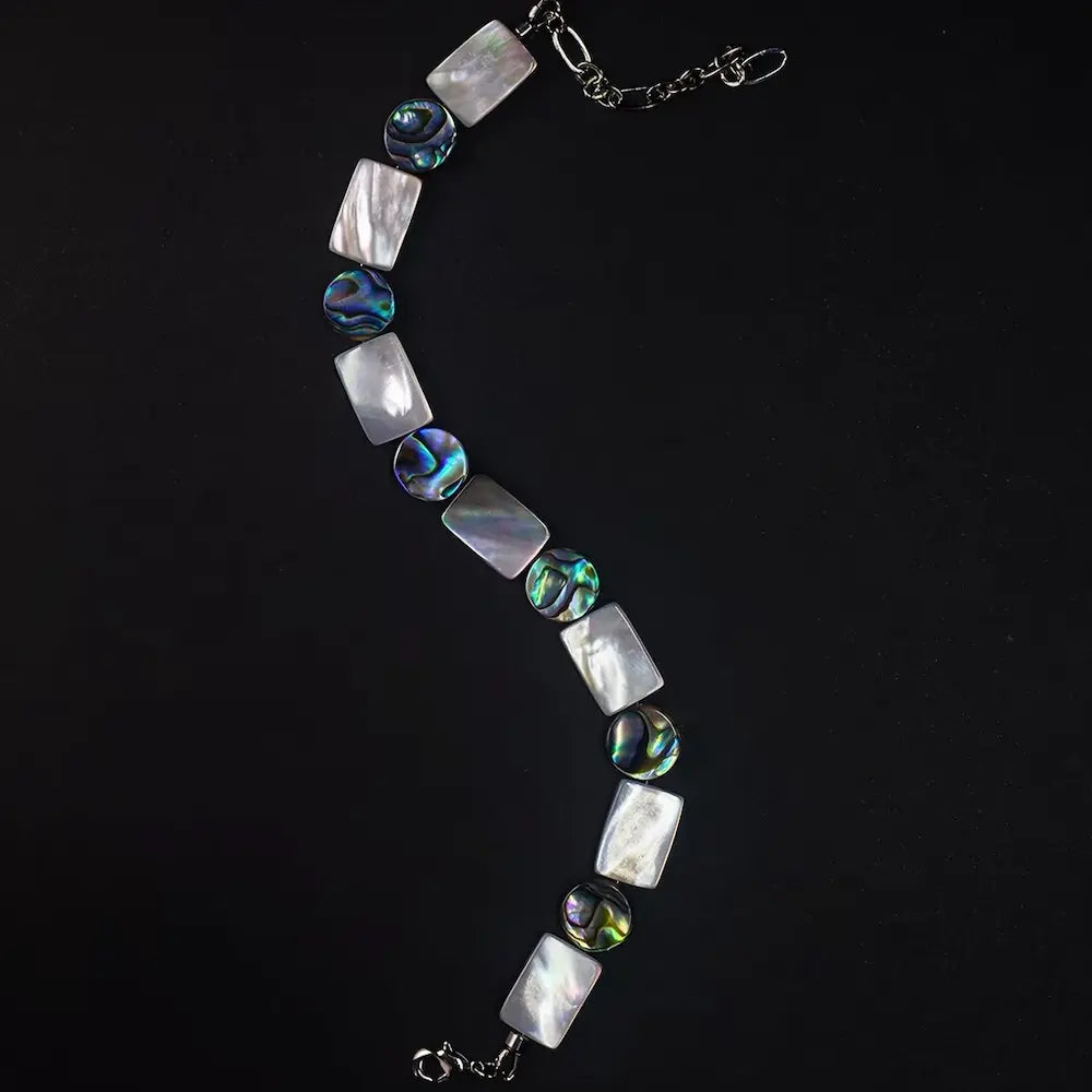 Full length view of Mother of Pearl and iridescent abalone shell beaded bracelet laid in an S-curve — Orienlu