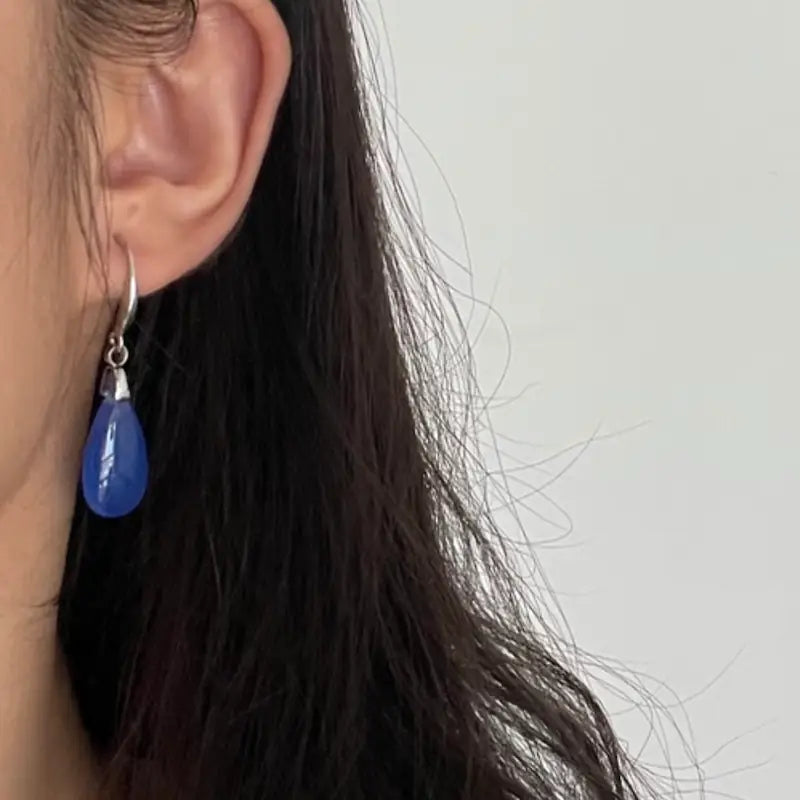 Close-up side profile of a woman wearing the Orienlu blue agate teardrop earring, demonstrating its delicate scale, minimalist drape, and how the jelly-textured blue chalcedony stone catches the light.