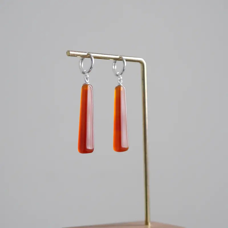 A front-view detail shot of the Orienlu red carnelian agate drop earrings, showcasing the smooth geometric cut of the gemstones and the silver-plated hardware.