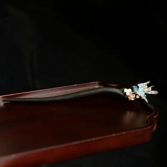 Orienlu official main product image of a neo-Chinese style sandalwood hair stick, featuring an intricate cloisonne blue bird charm, delicate shell pearls, and a dangling agate tassel, resting on a vintage wooden tray.