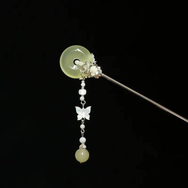 Studio view of the Orienlu gemstone hair stick showing the reverse construction, focusing on the alloy floral metalwork securing the pale green chalcedony disc and the link chain alignment.