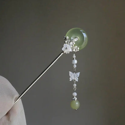 Close-up shot of the 16cm hair stick held in hand under soft ambient lighting, highlighting the organic iridescence of the carved shell butterfly and the translucent clarity of the agate stones.