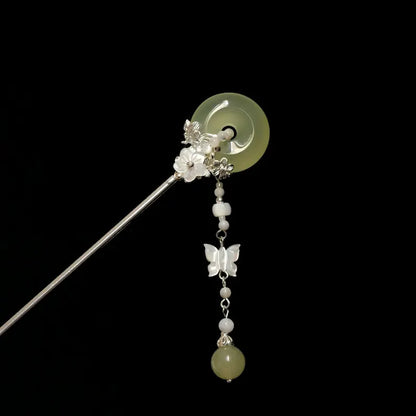 Orienlu product shot of a silver-toned hair stick against a solid black background, showcasing a translucent light green agate donut disc accented with a dangling mother-of-pearl butterfly tassel.
