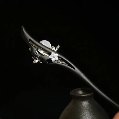 The reverse side view of the Orienlu hair pin inserted in a ceramic vase, revealing a delicate carved white shell flower embedded seamlessly within the hollow ebony frame.