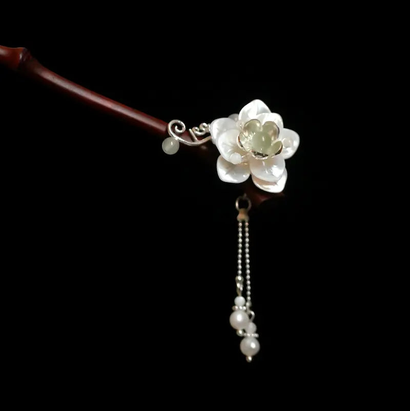 A studio close-up of the Orienlu bamboo hair stick head against a black background, showcasing the iridescent shell flower petals, green nephrite jade center, and fine silver dangles.
