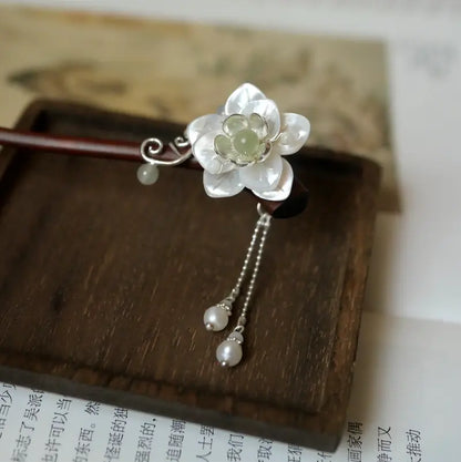An exquisite micro close-up focusing on the layers of natural mother of pearl shell craft and the smooth, round freshwater pearl drop tassels on a wooden stand.