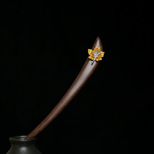 A striking studio shot of the Orienlu red sandalwood hair pin resting elegantly in a dark ceramic vase against a moody black background, highlighting its sleek curved silhouette.