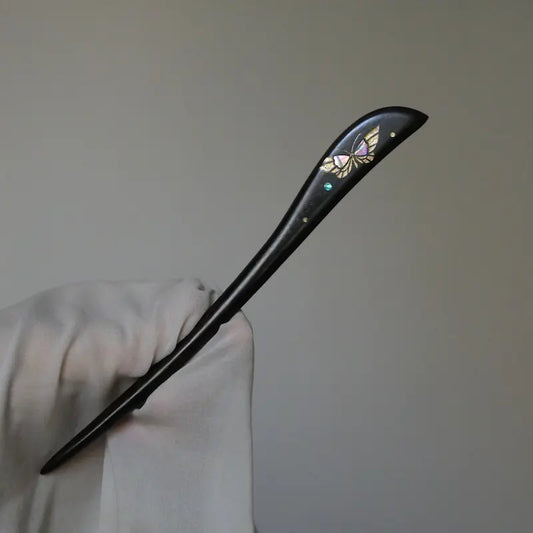 Orienlu official main product image of a neo-Chinese style ebony wood hair stick held by a gloved hand, showcasing an intricate hand-crafted mother of pearl butterfly inlay with elegant gold detailing.
