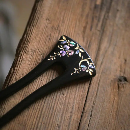 A macro close-up detail shot of the Orienlu ebony wood hair stick, showcasing the iridescent pink and green shifting colors of the floral shell inlay artwork resting on a rustic wooden surface.