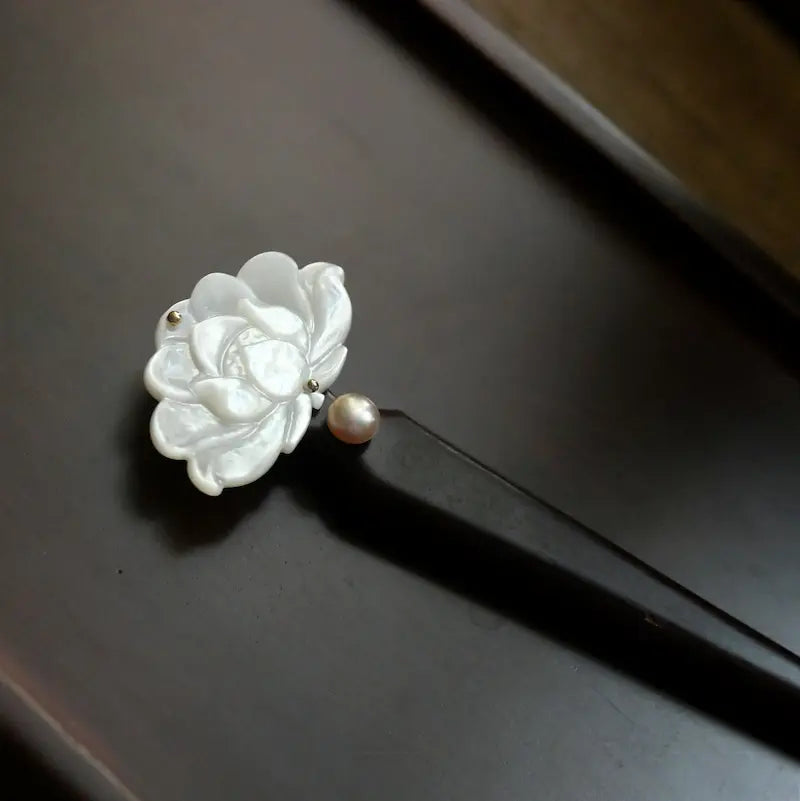 An exquisite close-up shot of the hair pin head, highlighting the intricate 3D carved details of the shell flower petals and the metallic luster of the pink-toned pearl.