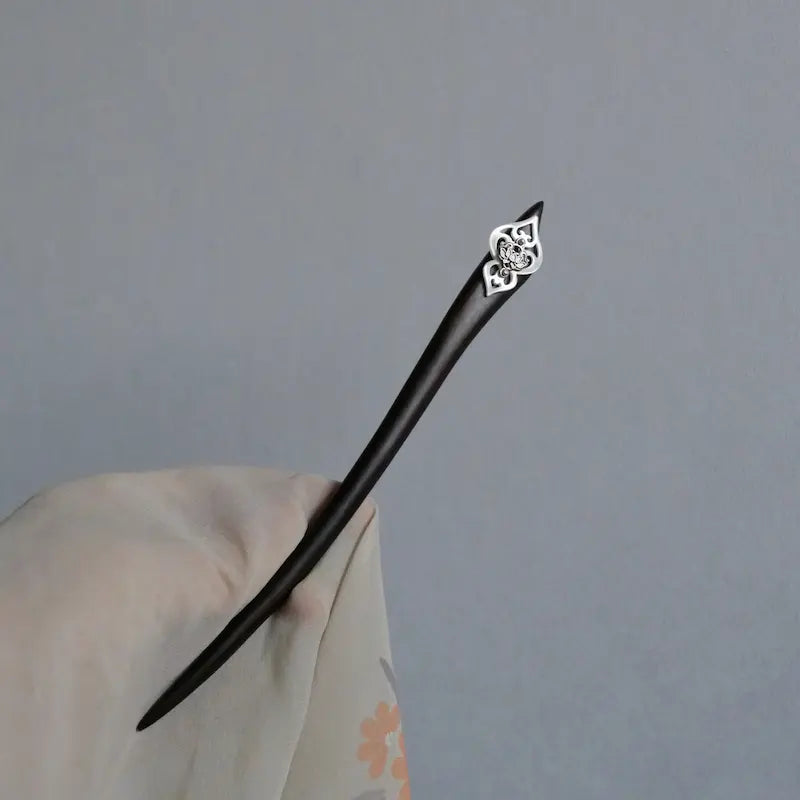 A hand-held view of the full-length tapered ebony wood hair stick, draped in translucent linen fabric to demonstrate its sleek architectural profile.
