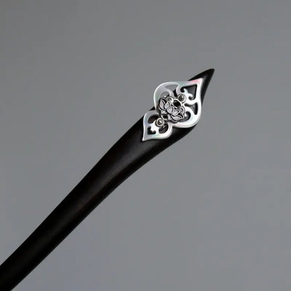 An overhead macro studio shot focusing on the geometric cut of the black timber hair pin topped with solid silver craftsmanship and a carved white shell base.