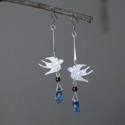 Silver mother of pearl swallow drop earrings with garnet beads and blue crystal teardrops hanging on a rustic branch — Orienlu