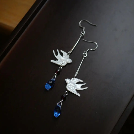 Handcrafted mother of pearl swallow drop earrings with red garnet and blue glass teardrop on dark wooden background — Orienlu