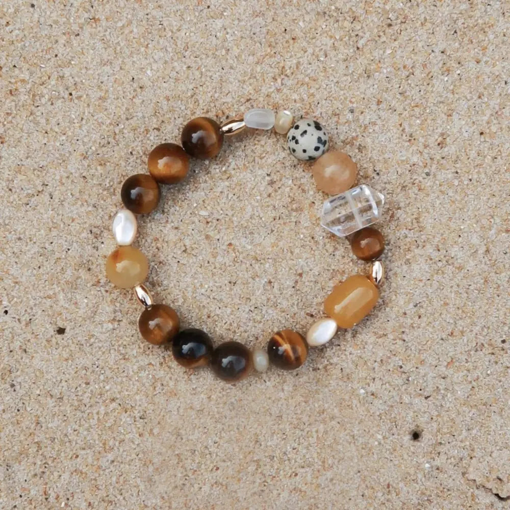 Handcrafted tiger eye multi-stone bracelet with golden silk jade, mother of pearl, and white crystal on sand background Orienlu