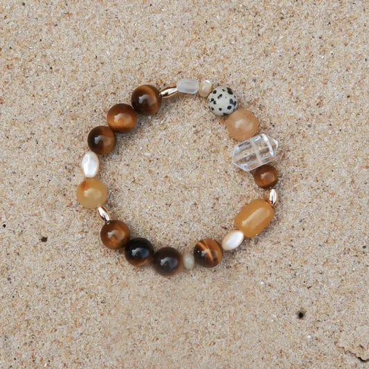 Handcrafted tiger eye multi-stone bracelet with golden silk jade, mother of pearl, and white crystal on sand background Orienlu