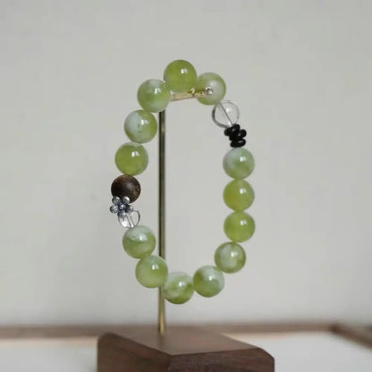 Chinese zen beaded bracelet featuring green xiuyu jade and agarwood on a gold-toned jewelry display stand
